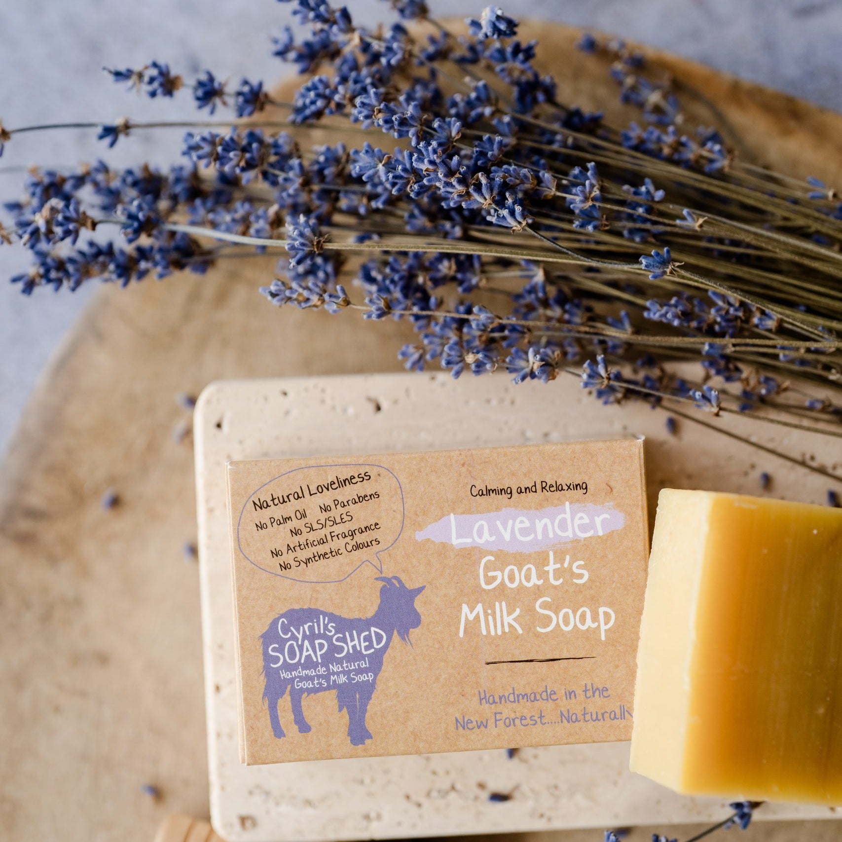Bar of goat's milk soap with a label, surrounded by lavender flowers on a wooden board.