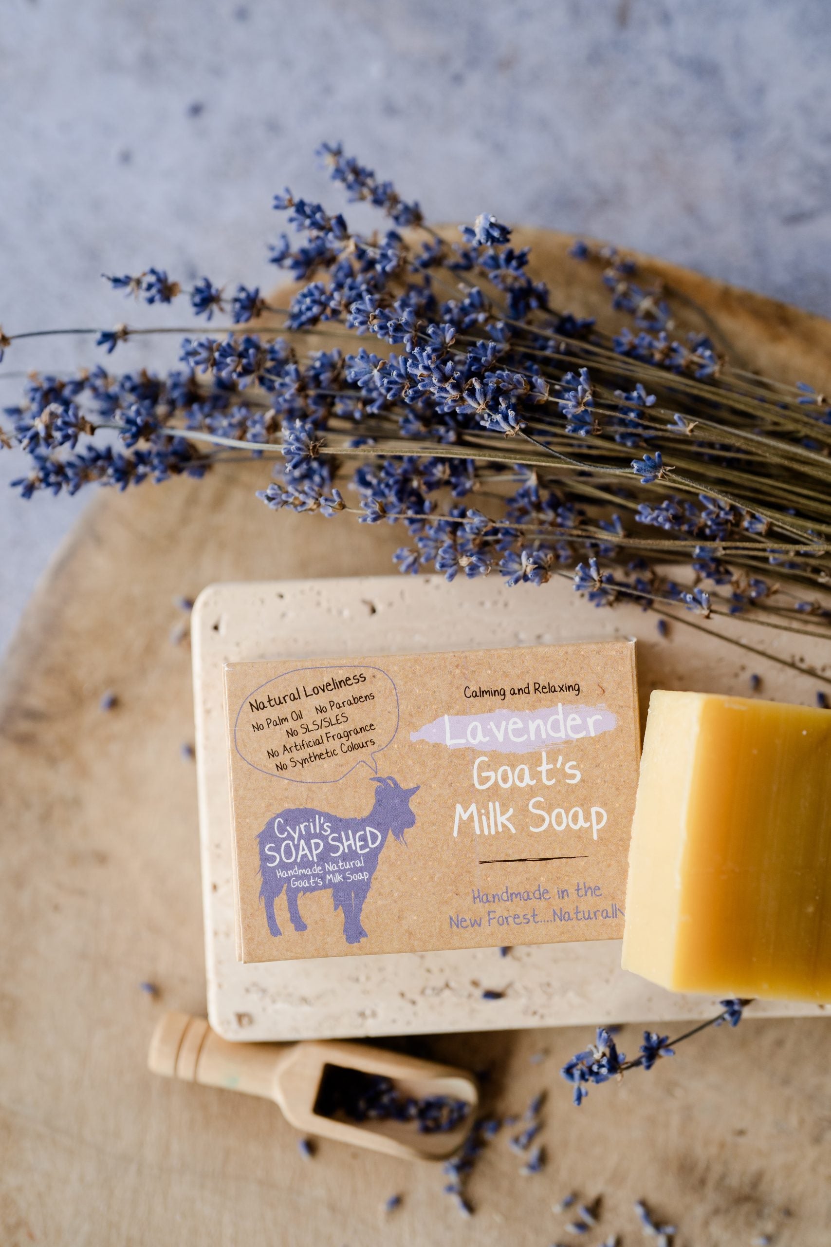 Bar of goat's milk soap with a label, surrounded by lavender flowers on a wooden board.